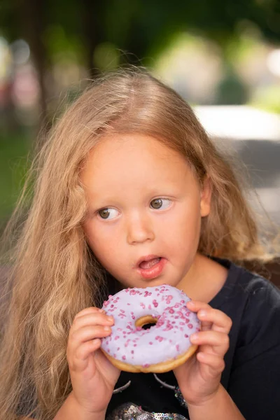 bir sandalyede oturuyor ve mor çörek yemek güzel sevimli küçük kız