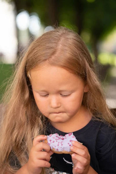 かわいい美しい少女椅子に座っていると 紫のドーナツを食べる — ストック写真