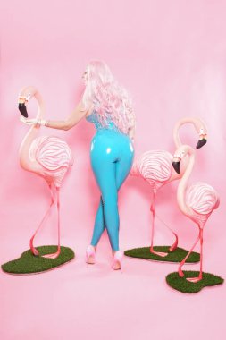 Sevimli tombul kız pembe studio arka plan üzerinde büyük bir Flamingo ile poz parlak mavi lateks mayo giymiş