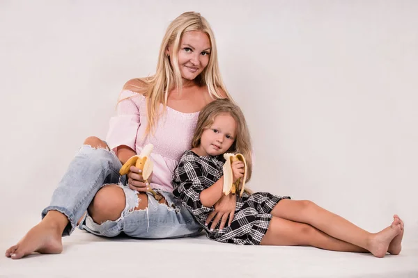 cute close-knit family mom and daughter sit and eat banana on white background