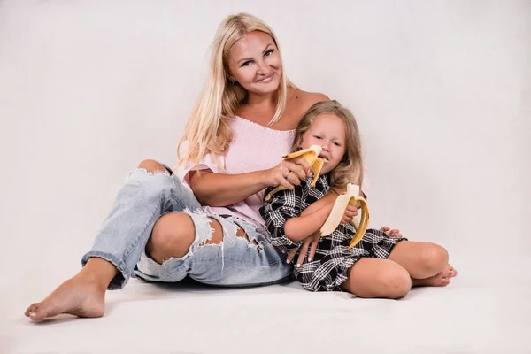 cute close-knit family mom and daughter sit and eat banana on white background