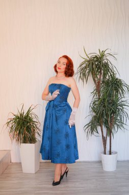 Boş beyaz odada tek başına duran mavi retro elbiseli huylu güzel vintage kadın giyinmiş