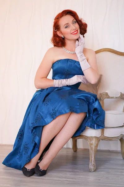 Yalnız ve beyaz arka plan üzerinde gülümseyen bir sandalyede oturan mavi retro elbise giymiş huylu vintage kadın güzel