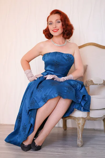 Yalnız ve beyaz arka plan üzerinde gülümseyen bir sandalyede oturan mavi retro elbise giymiş huylu vintage kadın güzel