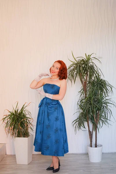 Boş beyaz odada tek başına duran mavi retro elbiseli huylu güzel vintage kadın giyinmiş