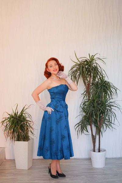 Boş beyaz odada tek başına duran mavi retro elbiseli huylu güzel vintage kadın giyinmiş