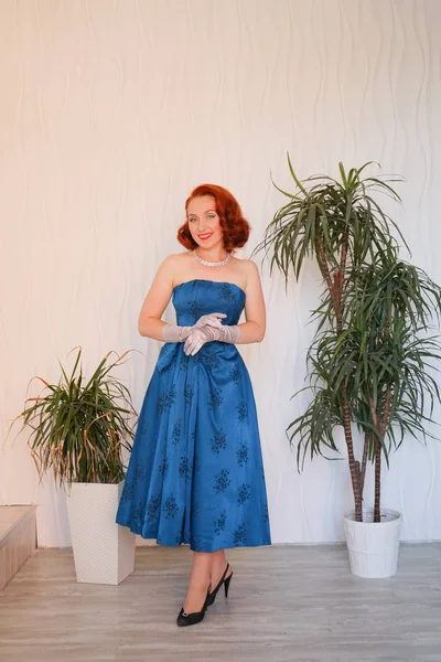 Boş beyaz odada tek başına duran mavi retro elbiseli huylu güzel vintage kadın giyinmiş