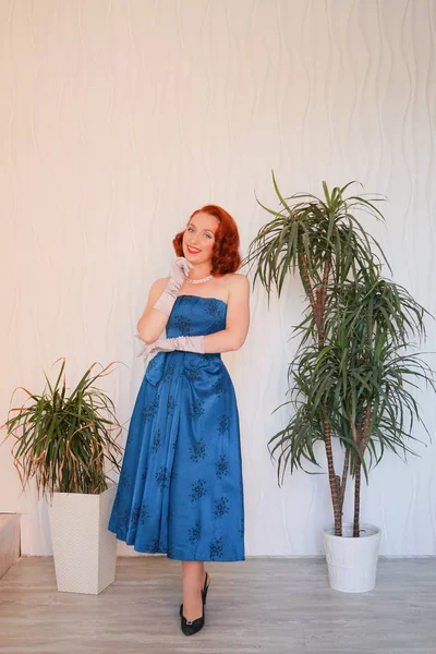 Boş beyaz odada tek başına duran mavi retro elbiseli huylu güzel vintage kadın giyinmiş