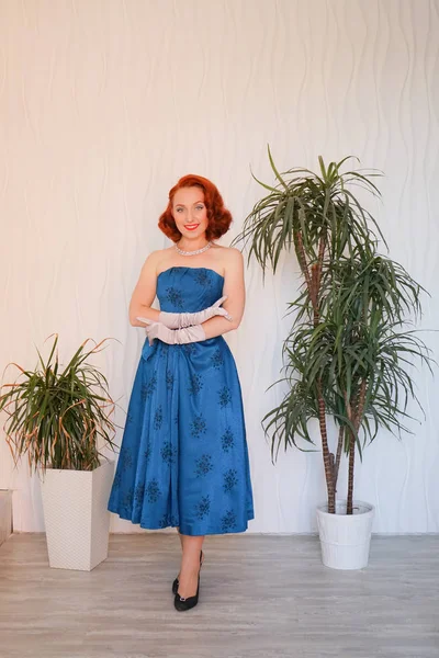 Boş beyaz odada tek başına duran mavi retro elbiseli huylu güzel vintage kadın giyinmiş