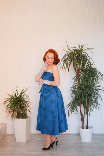 Boş beyaz odada tek başına duran mavi retro elbiseli huylu güzel vintage kadın giyinmiş