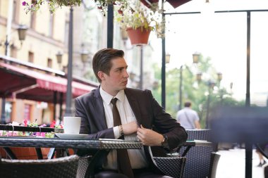 Genç bir işadamı bir sokak kafede yemeğe geldi, bir masada oturur ve faturayı ödemeyi bir çanta çeker