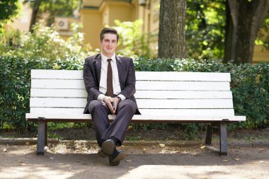 Yorgun bir adam bir takım elbise içinde ofis sol ve parka gitti. o yalnız bir beyaz bankta oturan ve birisi bekleyin.