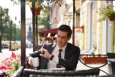 Genç bir adam bir siyah takım elbise, beyaz gömlek ve kravat saate benziyor