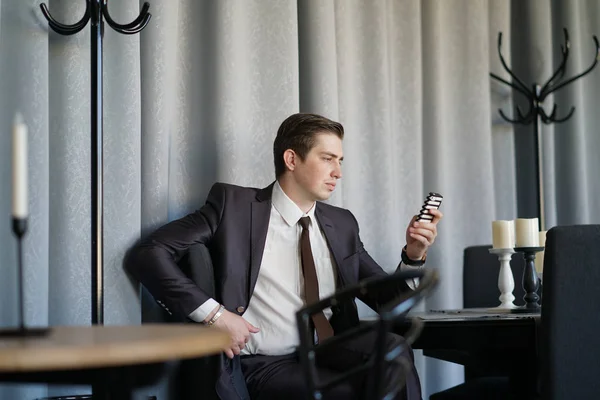 a young man in a black business suit, white shirt and tie looking at the news feed on the phone