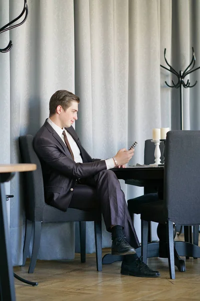 a young man in a black business suit, white shirt and tie looking at the news feed on the phone