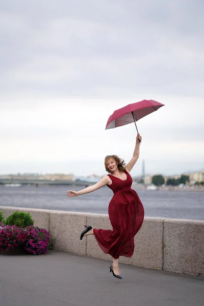 Веселая Смеющаяся Девушка Вишневом Длинном Платье Прыгает Бегает Зонтиком Фоне — стоковое фото