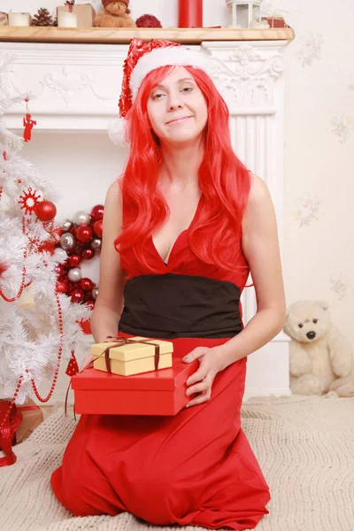 暖炉と赤いロング ドレス 黒の靴下 ホリデイ 帽子の白いクリスマス ツリーの近くポーズすっぴん背の高い細い女の子 — ストック写真