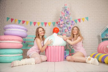 iki şirin arkadaşlarım Pembe pijama yere oturup zevk ve hediyeler ile Noel ağacı yakınındaki gülüyor