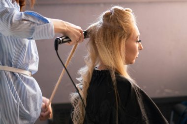 yaparken bir Kuaför ana salonda bir oluklu ve bir perma saçları güzel yetişkin sarışın istemci bir sandalyede oturur