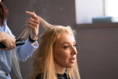 yaparken bir Kuaför ana salonda bir oluklu ve bir perma saçları güzel yetişkin sarışın istemci bir sandalyede oturur