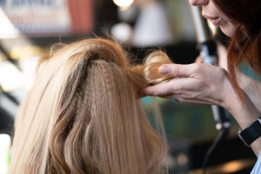 yaparken bir Kuaför ana salonda bir oluklu ve bir perma saçları güzel yetişkin sarışın istemci bir sandalyede oturur