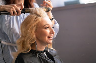 yaparken bir Kuaför ana salonda bir oluklu ve bir perma saçları güzel yetişkin sarışın istemci bir sandalyede oturur