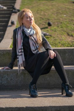 çok güzel sarışın kadın bir deri ceket, siyah elbiseli ve kareli bir bej eşarp ile şehir etrafında yürür ve olumlu hayatına sahiptir