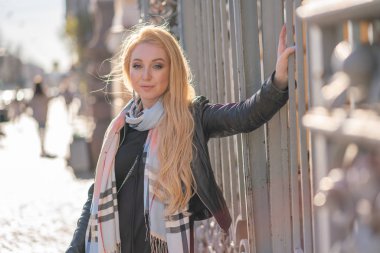 çok güzel sarışın kadın bir deri ceket, siyah elbiseli ve kareli bir bej eşarp ile şehir etrafında yürür ve olumlu hayatına sahiptir