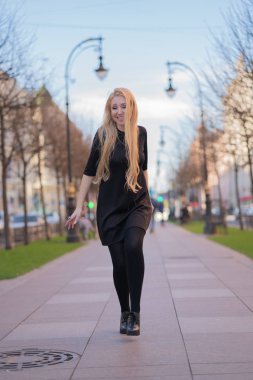 çok güzel sarışın kadın bir deri ceket, siyah elbiseli ve kareli bir bej eşarp ile şehir etrafında yürür ve olumlu hayatına sahiptir