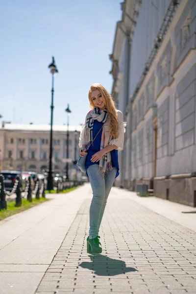 迷人的金发女孩 长头发 蓝色夹克和牛仔裤与米色格子围巾微笑着在城市的人行道上 享受一个阳光明媚的春日 — 图库照片
