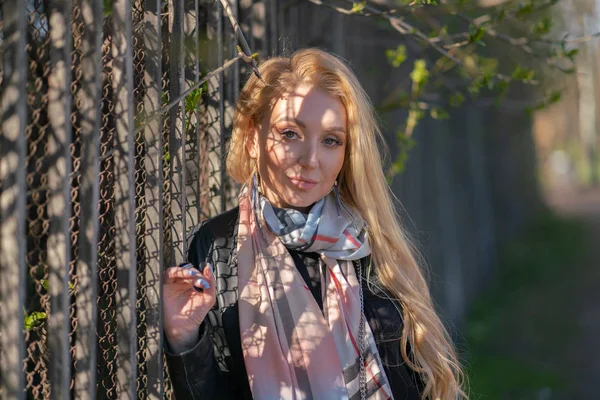 lovely blonde woman in a leather jacket, black dress and with a checkered beige scarf walks around the City and enjoys life on the positive