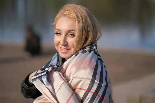 lovely blonde woman in a leather jacket, black dress and with a checkered beige scarf walks around the City and enjoys life on the positive