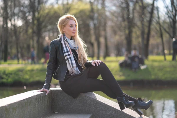 lovely blonde woman in a leather jacket, black dress and with a checkered beige scarf walks around the City and enjoys life on the positive