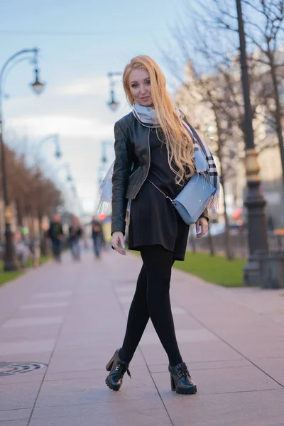 素敵な金髪女性の市松模様ベージュ スカーフと革のジャケット 黒のドレスで街を歩くし 積極的に人生を楽しんでいます — ストック写真