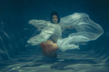 zarif ince kız su altında güzel kumaş ile beyaz gece elbisesi içinde ücretsiz bir dalgıç gibi yüzüyor