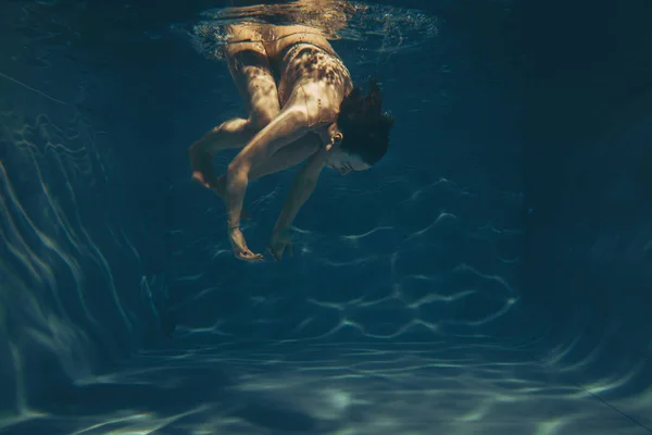 cute sporty girl swims underwater as a free diver in sheer jumpsuit alone