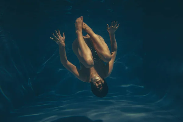 cute sporty girl swims underwater as a free diver in sheer jumpsuit alone