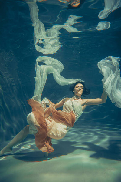 elegant slender girl swims underwater like a free diver in a white evening dress with beautiful fabric