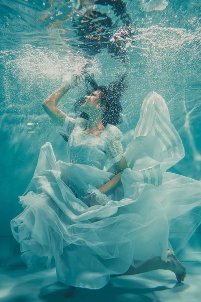性感的年轻新娘游泳在水下穿着白色婚纱 丝袜和手套 — 图库照片