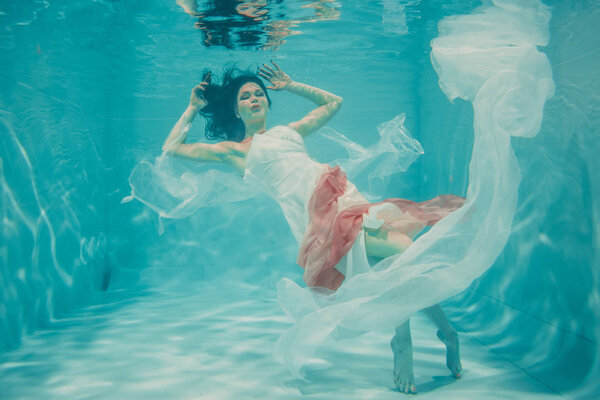 beautiful model girl swimming underwater in feminine long white and pink dress