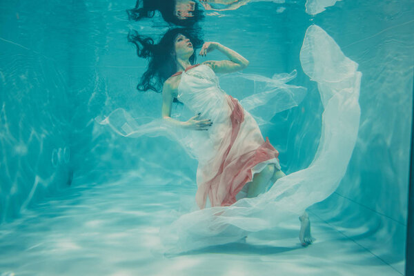 beautiful model girl swimming underwater in feminine long white and pink dress