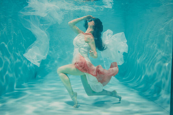 beautiful model girl swimming underwater in feminine long white and pink dress