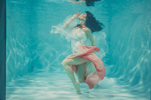 beautiful model girl swimming underwater in feminine long white and pink dress