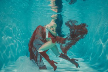 güzel seksi kız sualtı yüzme sportif stil kırmızı ve beyaz Fetiş korse ve dizine uyluk yüksek topuklu çizmeler.