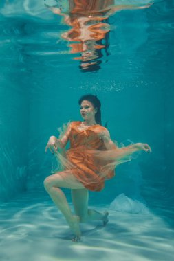 güzel model kız su altında Turuncu elbise içinde yüzüyor ve rahatlama ve stres eksikliği sahiptir