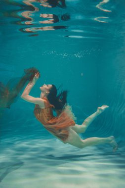 güzel model kız su altında Turuncu elbise içinde yüzüyor ve rahatlama ve stres eksikliği sahiptir