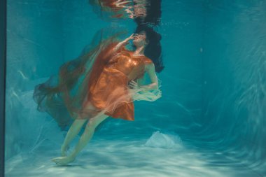 güzel model kız su altında Turuncu elbise içinde yüzüyor ve rahatlama ve stres eksikliği sahiptir