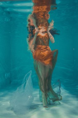 güzel model kız su altında Turuncu elbise içinde yüzüyor ve rahatlama ve stres eksikliği sahiptir