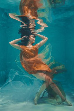güzel model kız su altında Turuncu elbise içinde yüzüyor ve rahatlama ve stres eksikliği sahiptir