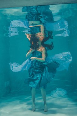 güzel model kız su altında mavi elbiseli yüzüyor ve rahatlama ve stres eksikliği sahiptir